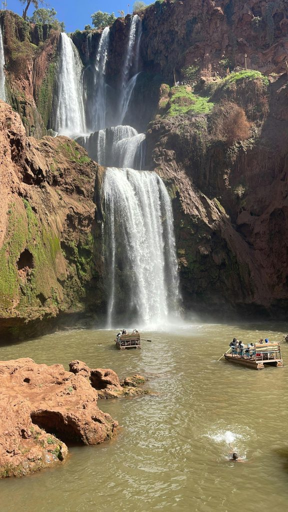 Capture of Ouzoud Waterfalls with tourists enjoying boat rides under the bright sun.
